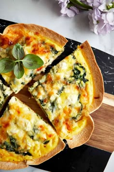 a quiche with cheese and spinach on a cutting board next to purple flowers