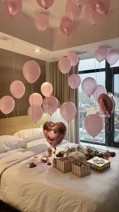 pink balloons are floating from the ceiling above a bed with gifts and presents on it