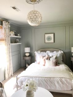 a white bed sitting in a bedroom next to a table and chair with a vase on top of it