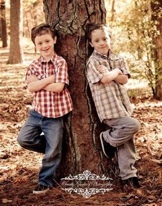 two young boys leaning against a tree in the woods