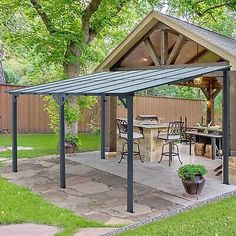 a covered patio with an outdoor kitchen and dining area in the back yard, surrounded by trees