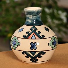 a ceramic vase sitting on top of a table next to a potted plant in the background