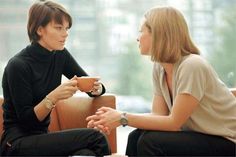 two women sitting on couches talking to each other while holding cups in their hands