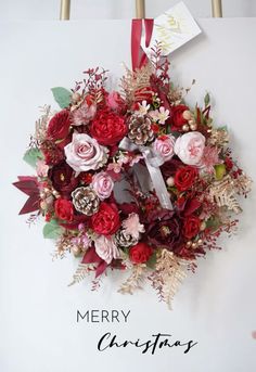 a merry christmas wreath hanging on the wall with red and pink flowers, greenery and pine cones