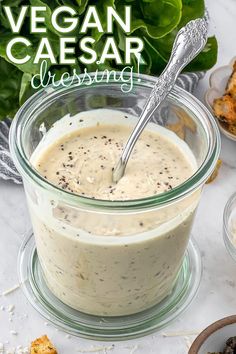 a glass jar filled with dressing next to other dishes and vegetables on a table top