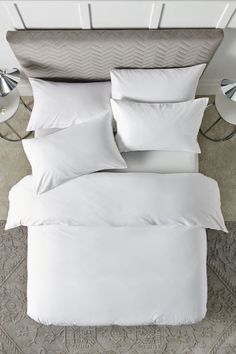 a bed with white sheets and pillows on top of it in a room that has carpeted flooring