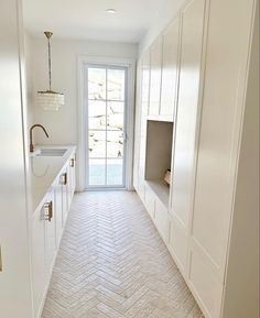 an empty kitchen with white cabinets and herringbone tile flooring, along with a door leading to the outside