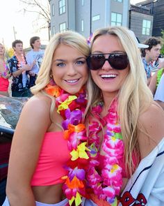 two beautiful young women standing next to each other in front of a car at a festival