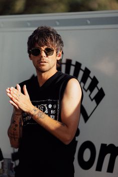 a man wearing sunglasses standing in front of a sign with his hands folded up to the side