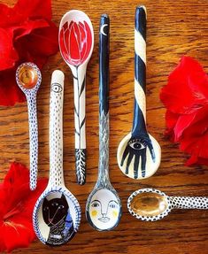 five spoons are lined up on a wooden table with red flowers in the background