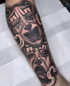 a man's leg with a black and grey tattoo design on it, featuring a mask