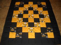 a black and yellow quilt with pittsburgh football patches on the center is laying on a wooden floor