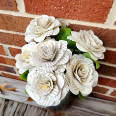 a vase filled with paper flowers sitting on top of a wooden table next to a brick wall