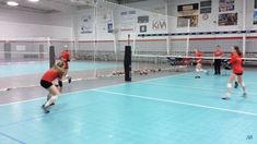 some girls are playing volleyball in a gym with blue tiles on the floor and white net