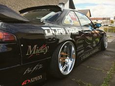 the back end of a black sports car parked in front of a building with graffiti on it