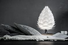 a white lamp sitting on top of a wooden table next to pillows and coffee cup