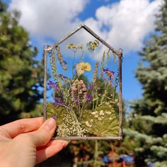 a hand holding up a glass house with flowers in it