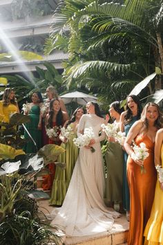 a group of women standing next to each other in front of plants and umbrellas