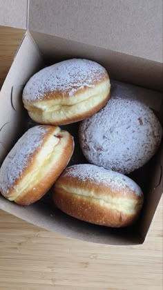 four donuts in a box with powdered sugar on top, sitting on a wooden table