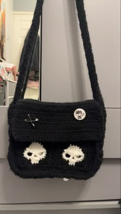 a black crocheted purse with eyes on the front hanging from a hook in a closet