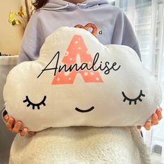 a person holding a pillow with the letter a on it that has eyes and eyelashes