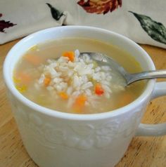 a white bowl filled with rice and carrots on top of a wooden table next to a pillow