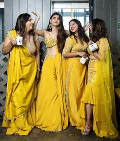 four women dressed in yellow posing for the camera with their arms around each other and holding coffee mugs