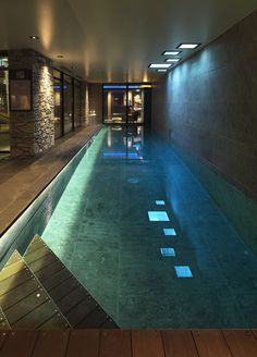 an indoor swimming pool with steps leading up to the water's edge and lights on