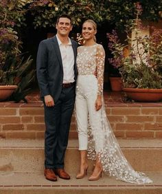 a man and woman standing next to each other in front of some potted plants