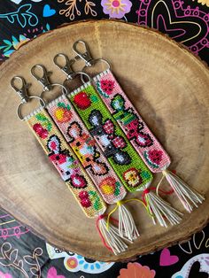 three cross stitch keychains sitting on top of a wooden slice