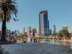 people are standing on the beach in front of some tall buildings