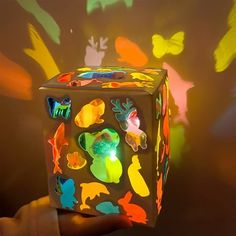 a hand is holding a lit up box with many different colored images on the surface