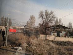 a fenced in area with barbed wire and people walking by it on a cloudy day