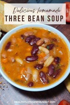 a bowl of bean and vegetable soup on a table with bread, tomatoes, and other vegetables