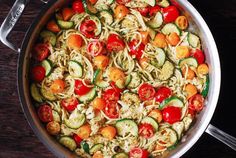 a pan filled with pasta and veggies on top of a wooden table