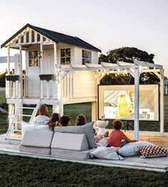 four people sitting on the back of a couch in front of a house with a tv