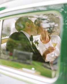 a bride and groom kissing in the back seat of a car while holding wine glasses