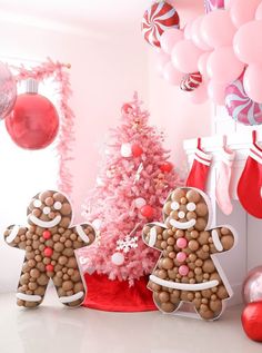 gingerbread man and woman standing in front of a pink christmas tree with balloons on the wall