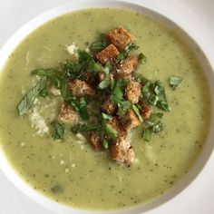 a white bowl filled with broccoli soup and croutons