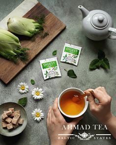 a person holding a cup of tea next to some flowers and other items on a table