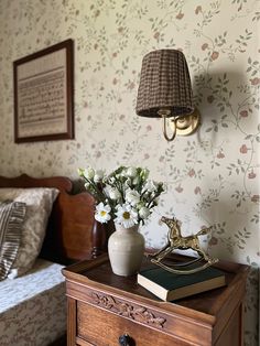 a nightstand with flowers and a lamp on it in a bedroom next to a bed