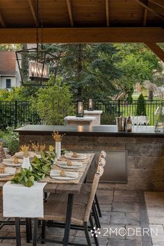 an outdoor kitchen and dining area with table set for four, grill in the background