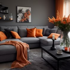 a living room with grey couches and orange throw pillows on the sofa, coffee table