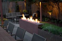 a fire pit in the middle of a patio with chairs around it and lights on