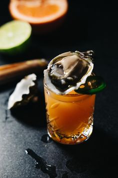 a glass filled with an alcoholic drink next to sliced oranges and lime wedges