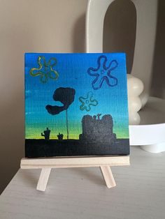 an acrylic painting on a wooden easel sitting on top of a table