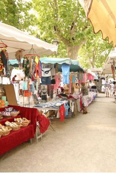 an outdoor market with umbrellas and tables full of goods for sale on the sidewalk