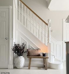 a white staircase with chandelier and bench