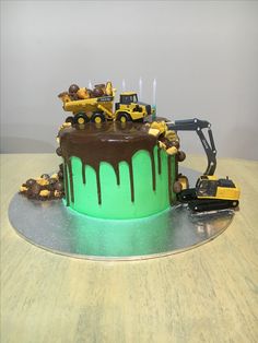 there is a green cake with chocolate icing and construction trucks on it, sitting on a table