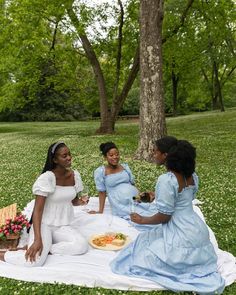 three women are sitting on a blanket in the grass and having a picnic with each other